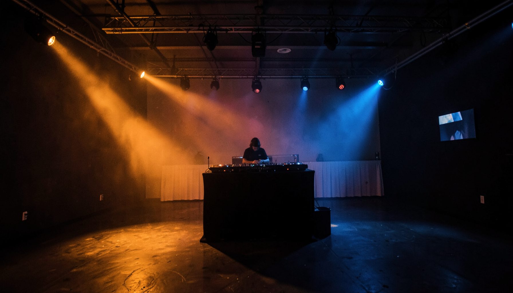 A darkened event space with dramatic orange, blue, and red beams of light cutting across an empty room, evoking the energy of a live mobile entertainment setup